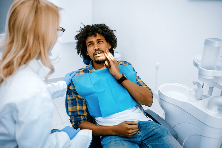 man sitting in dental chair holding cheek