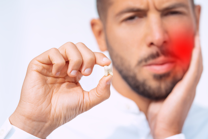 man holding a tooth and his cheek in pain